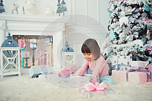 Positive cheerful baby girl sitting with Christmas gift near Christmas tree. Happy New Year