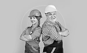 positive child and grandfather builder in helmet on yellow background