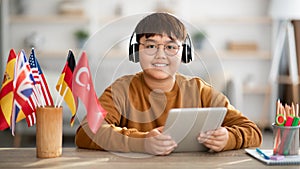 Positive chinese kid with wireless headset and digital tablet