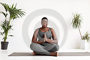 Positive chubby black woman doing yoga exercise at home