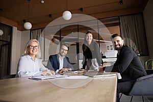 Positive confident business colleagues sitting, standing at meeting table