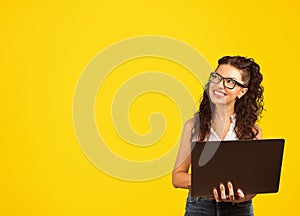 Positive cool lady with curly hair holding laptop looding away daydreaming