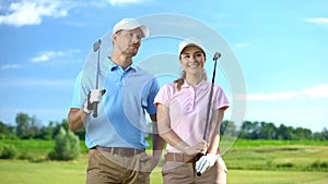 Positive couple of golfers holding clubs looking at course, sport game, career