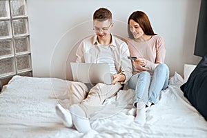 Positive couple looking at their accounts online sitting on the bed at home