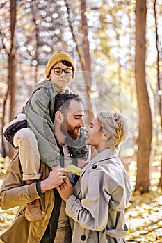 positive couple with son hugging kissing and having fun in autumn park or forest