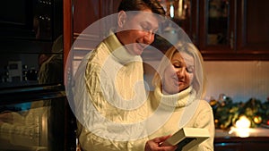 Positive couple talking admiring old photo in hands standing in kitchen at home. Portrait of Caucasian man and woman