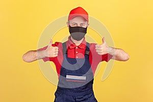 Positive crafts man in red and blue uniform and protective facial mask showing thumbs-up, satisfied with quality service during