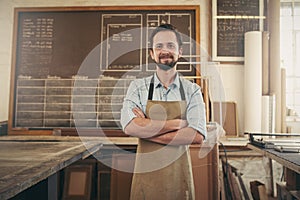 Positive craftsman in his workshop with arms folded