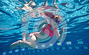 Positive, cute, little baby girl, toddler in pink swimsuit and goggles diving, swimming underwater in swimming pool