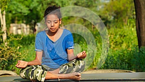 Positive cute little Indian girl sitting on the roll mat. Girls doing gymnastic exercises or exercising at outdoor