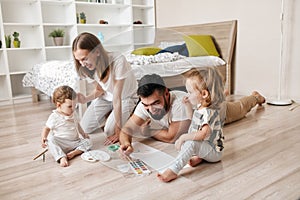 Positive dad, mommy, kids painting with brushes while sitting on the floor