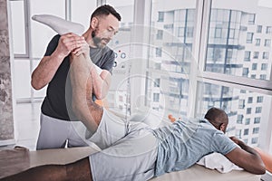 Positive delighted practitioner stretching leg of his patient