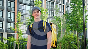 Positive deliveryman worker wears t-shirt and cap on background modern building