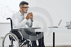 Positive disabled young man in wheelchair working in office