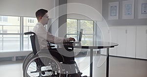 Positive disabled young man in wheelchair working in office