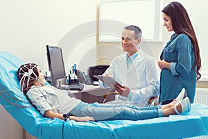 Positive doctor and mother talking to girl undergoing electroencephalography photo