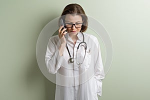 Positive doctor woman talking mobile phone. Background green wall in the clinic