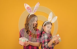 positive easter children in bunny ears hold gift box on yellow background