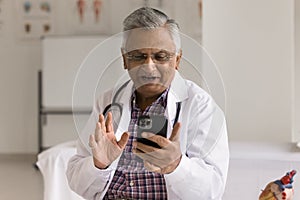 Positive elderly Indian medical professional man talking on video call