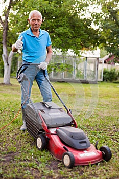 Positive elderly man with lawnmower when mowing the lawn