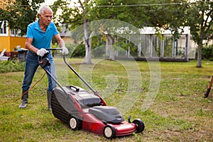 Positive elderly man with lawnmower when mowing the lawn