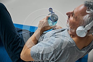 Positive elderly man with a water bottle listening to music