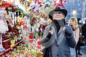 Positive elderly woman in festive mood walking on street Christmas fair