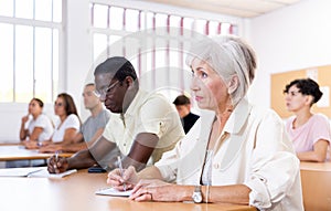 Positive elderly woman listening and taking notes during language courses