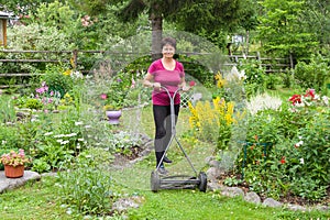 Positive elderly woman mowing grass with lawn mower in the garden