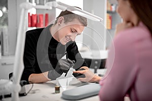 Positive emotional manicurist smiling while working with client