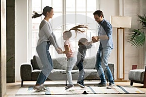 Positive energetic young parents dancing with little kids.