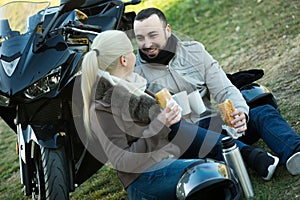 Couple posing near motor bike with sandwitches and coffee