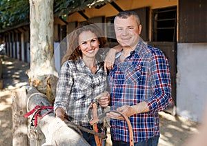 Positive family couple with belly-band standing at stable outdoor