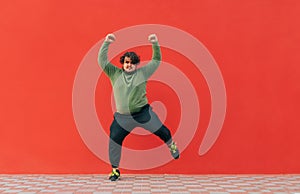 Positive fat dancer in casual clothes shows a performance on the street on a red background. Funny fat man dancing against the red