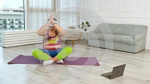 Positive fat man with virtual glasses doing yoga exercises. Plus size body positive practice yoga with laptop at home