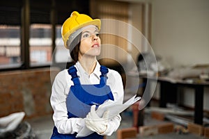 Positive female civil engineer taking notes while checking indoor construction site, satisfied with progress of work