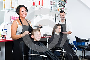 Positive female hairdresser cutting hair smiling boy