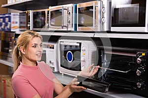 Positive female looking new microwave for kitchen in furniture store