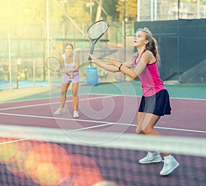 Positive female player hits ball close to net while playing tennis in rays of sun and glare