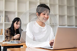 A positive female student is using her laptop while listening to a teacher lecture in the classroom