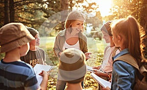 Positive female teacher interacting with school kids boys and girls during ecology lesson in forest