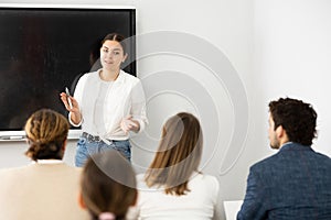 Positive female trainer standing near interactive board and conducting advanced training courses to office employees