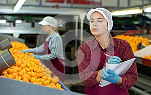 Positive female worker fills out a document at a citrus processing plant.