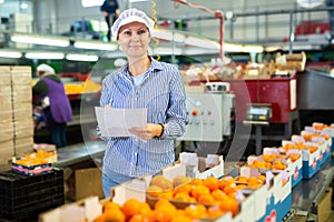 Positive female worker fills out a document at a citrus processing plant.