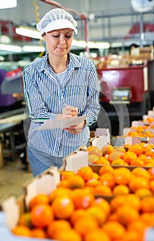 Positive female worker fills out a document at a citrus processing plant.