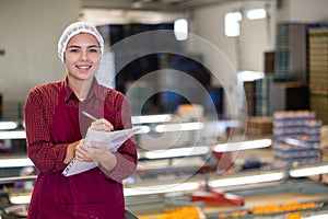 Positive female worker fills out a document at a citrus processing plant.