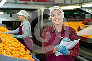 Positive female worker fills out a document at a citrus processing plant.