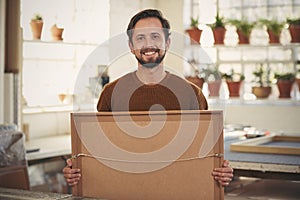 Positive framer smiling his workshop holding a framed item photo