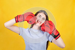 Positive and funny woman with red boxing gloves keeps fists to her cheeks. Portrait of confident girl smiling to camera isolated