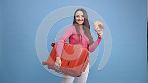Positive girl with baggage and money are going to travel. Woman in pink sweater and jeans standing on blue background